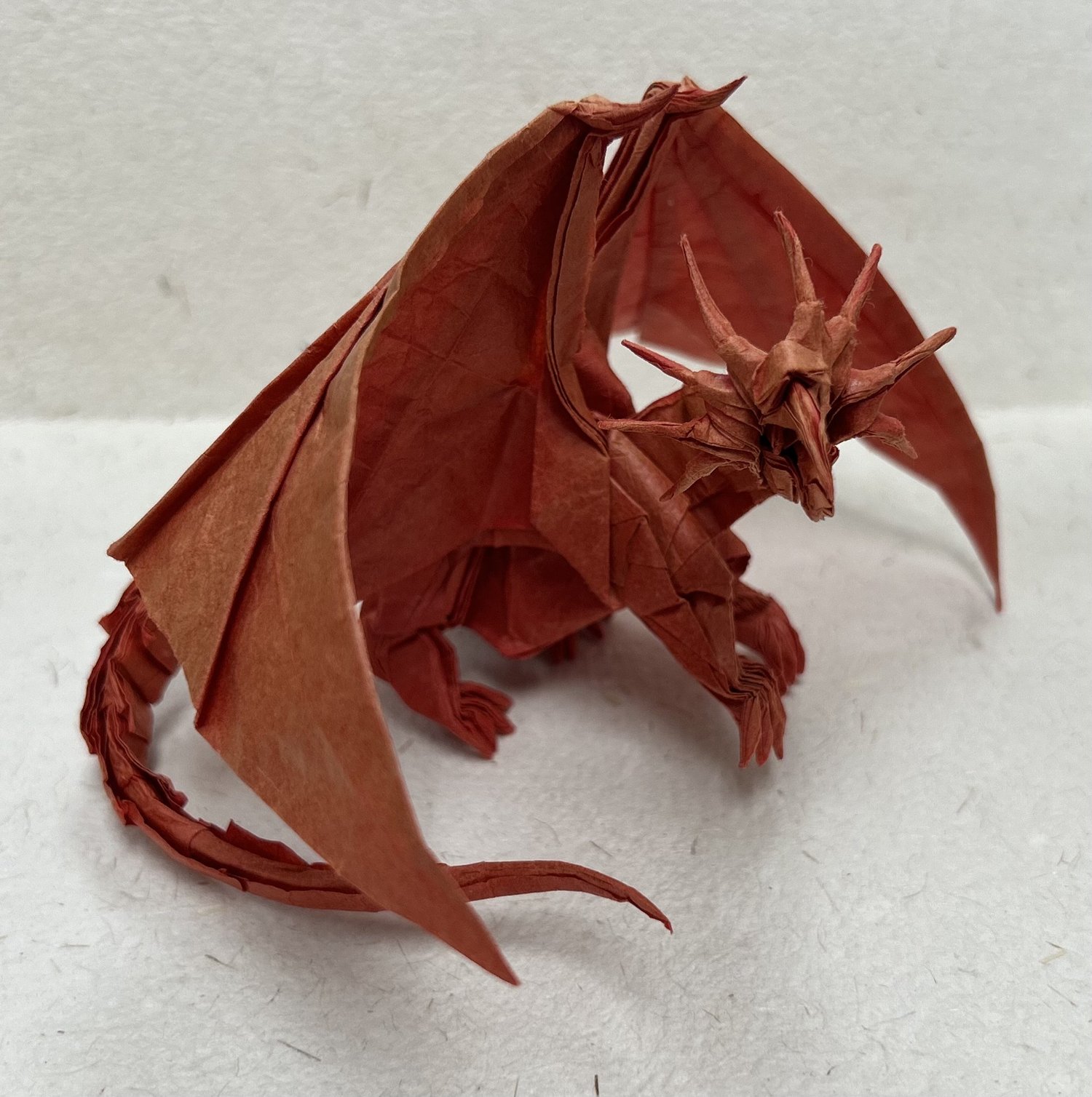 An origami dragon, hand-folded from red paper, wings spread